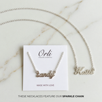 Sandy and Katie sterling silver name necklaces with sparkle chains, shown on and beside an Orli card.